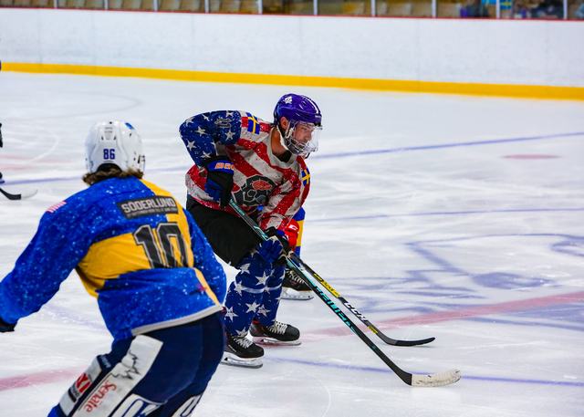 A USA skater in stars-and-stripes gear pressures a Sweden forward along the boards