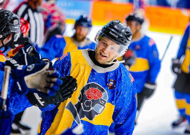 A grinning Sweden player skates through a scrum in front of the officials
