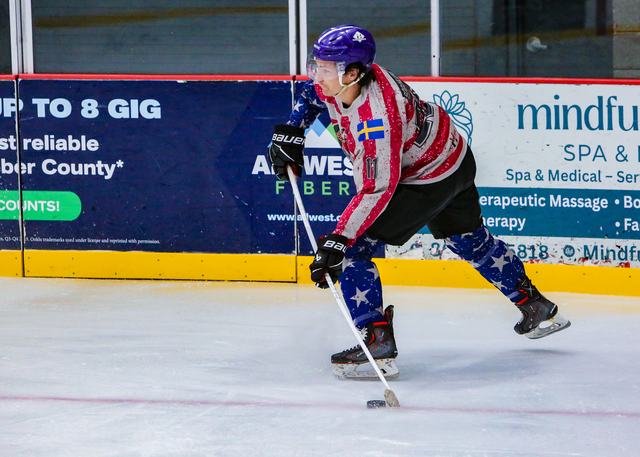 A USA forward carries the puck up the boards past the advertising panels